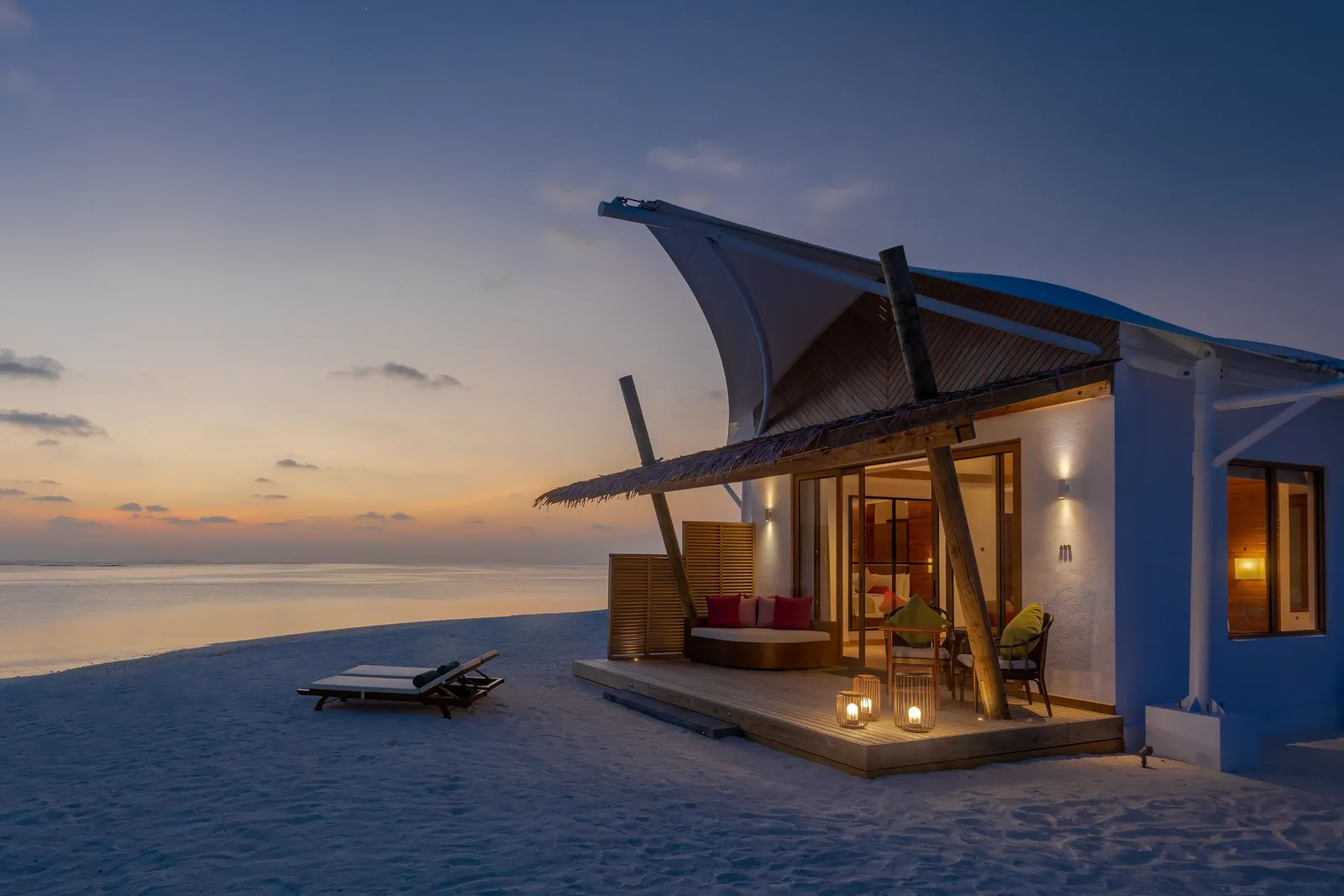 A Platinum Beach Bungalow at sunset, lanterns lit on the deck and 2 loungers on the sand