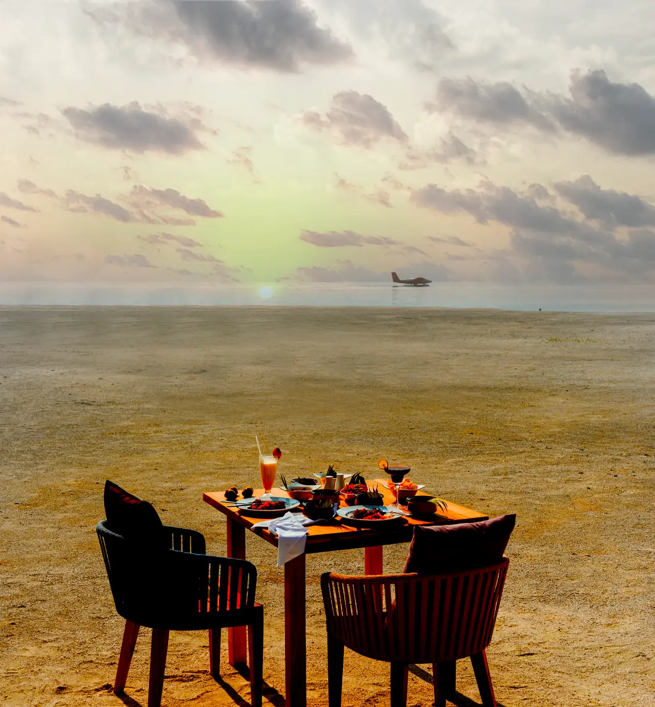 A table for 2 on a sandbank at sunset, a seaplane low on the horizon