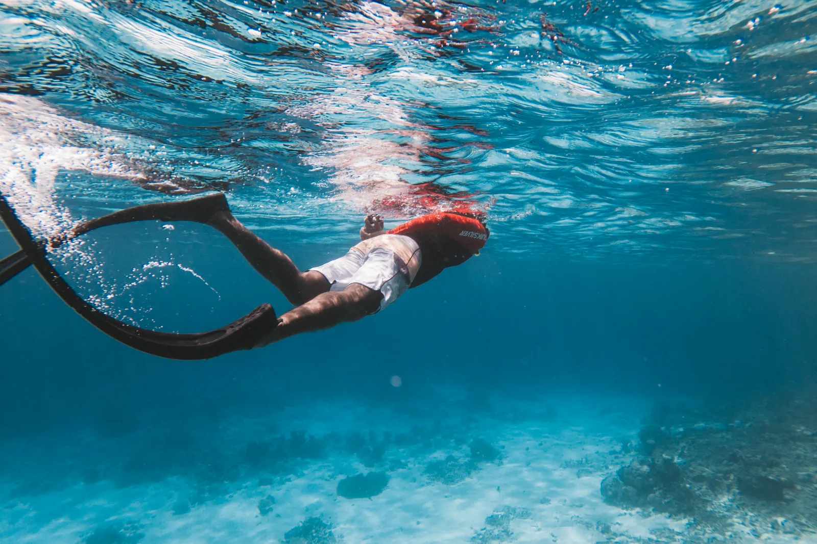 A freediver with long fins above a sandy seabed