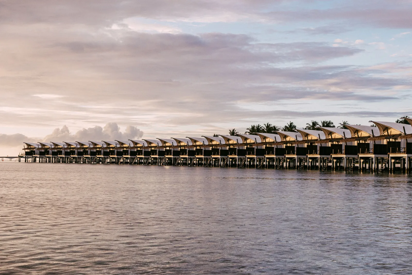 The row of water bungalows at dusk, their lights on above the lagoon