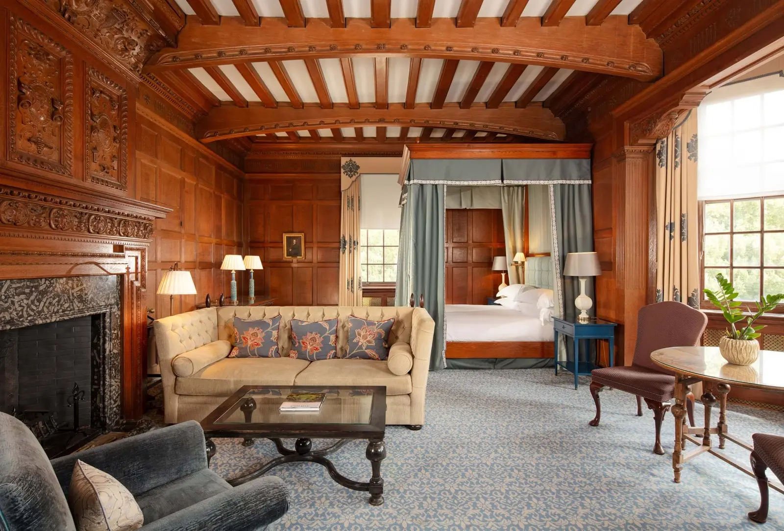 A Deluxe Suite: a painted beamed ceiling, oak panelling, a fireplace and a four-poster beyond