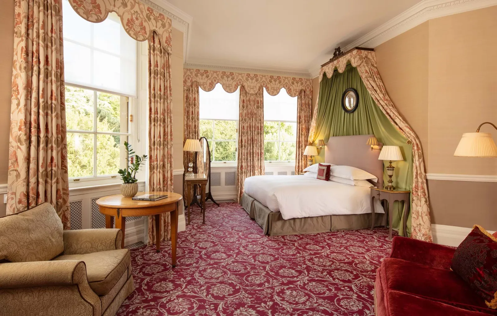 The Inchiquin Suite: a bed under a green canopy, a red carpet and a round table between 2 windows