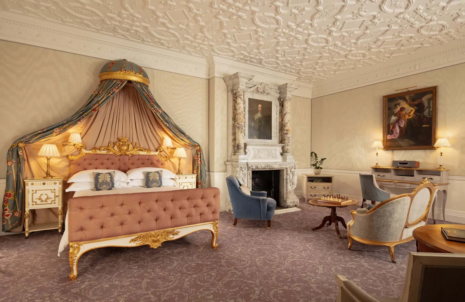 A Junior Suite: a gilded canopied bed, a moulded ceiling and a marble fireplace