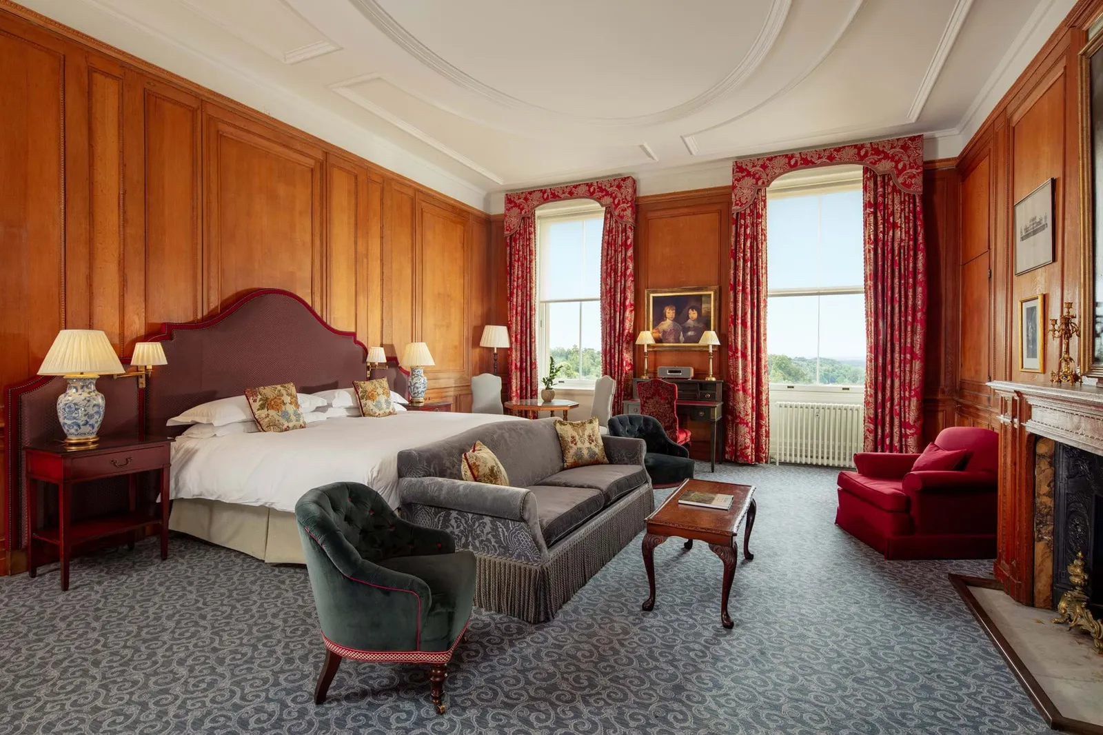 A Mansion House Deluxe Suite: wood-panelled walls, a bed with floral cushions and red armchairs