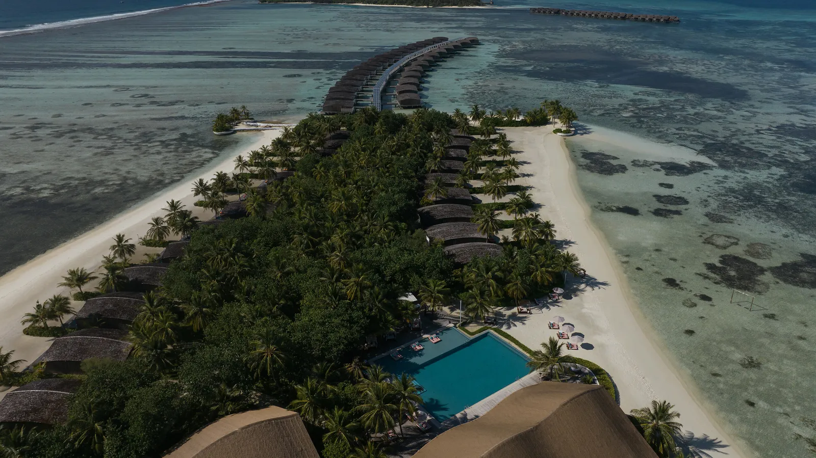 Gasfinolhu from the air: the strip of sand and green, the main pool, the beach villas and the jetty of water villas reaching into the lagoon.