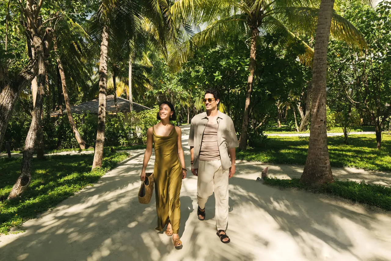 A couple walking along a sandy path between the palms and the island’s lawns.