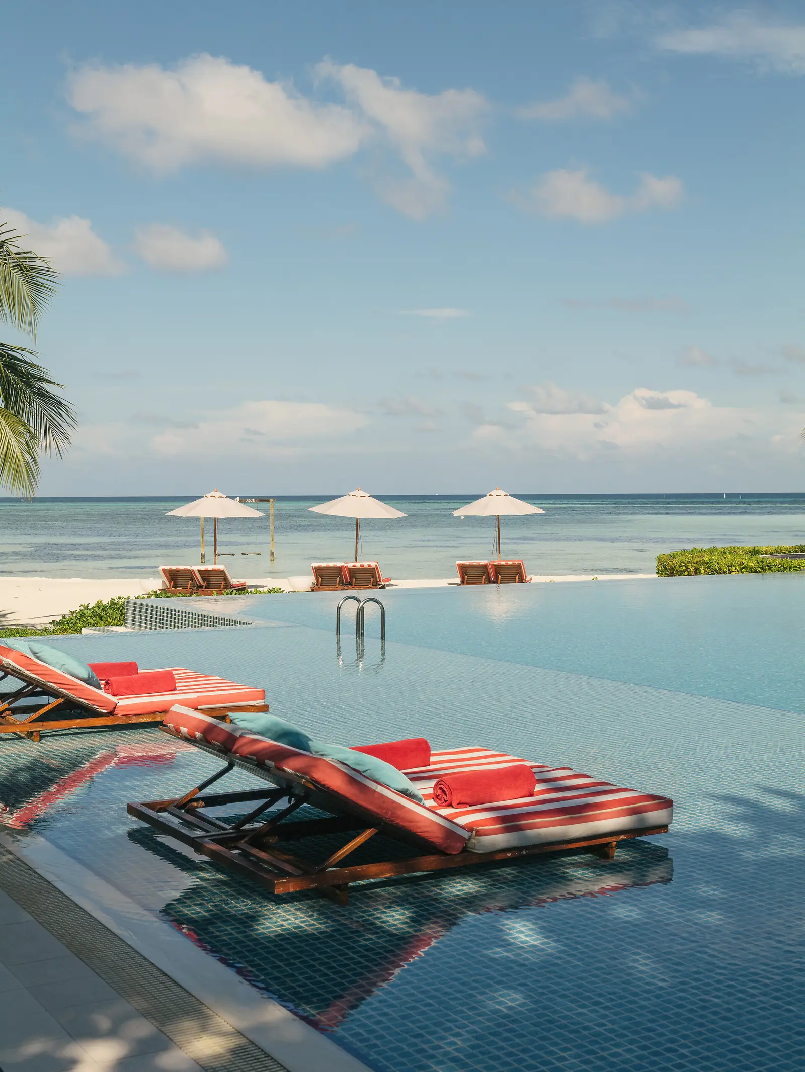Red-striped loungers in the shallow water of the main pool, with the parasols on the beach beyond the edge.