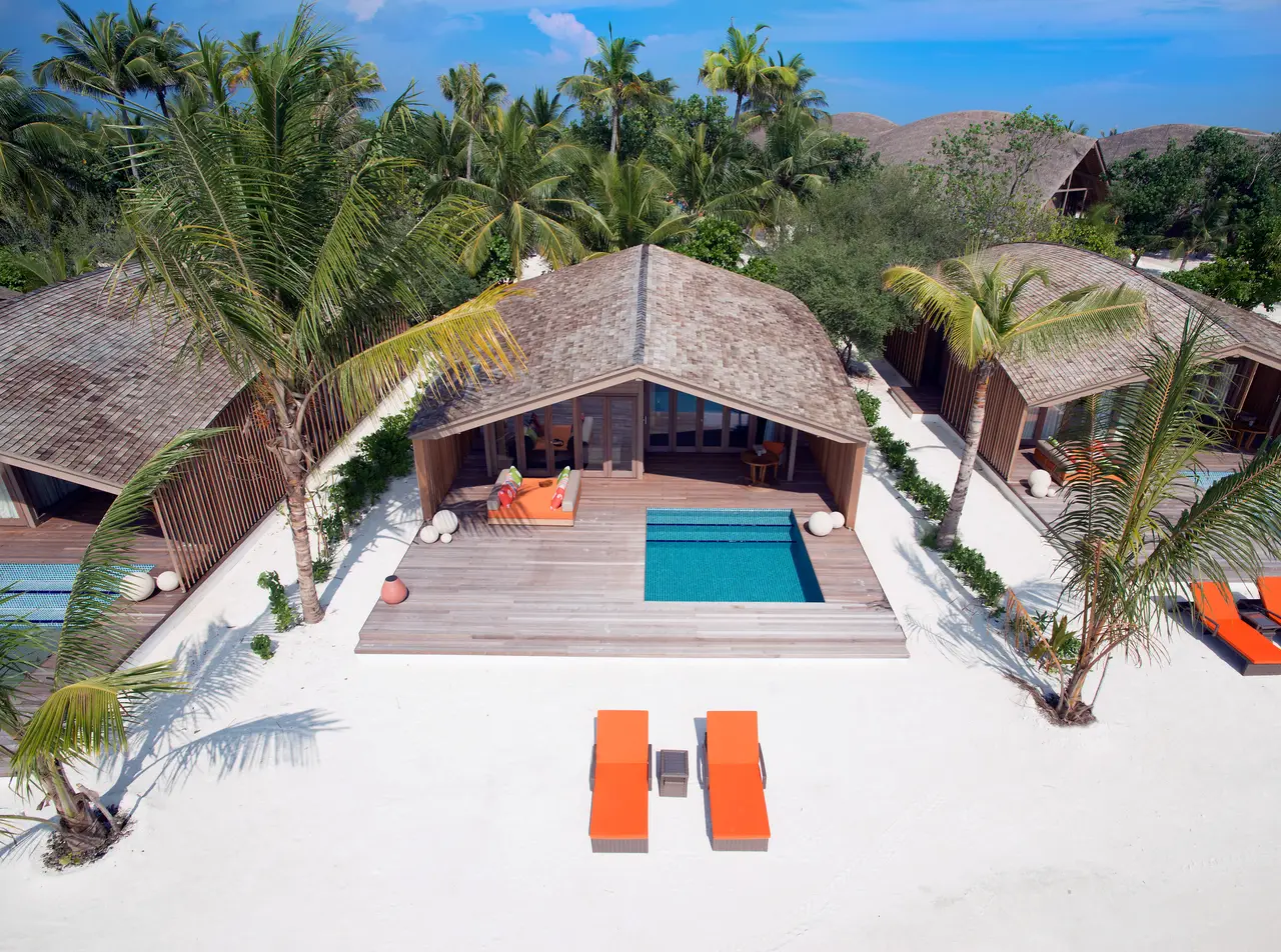 A Beach Villa from the air: the curved roof among the palms, the teak deck with its pool and 2 orange loungers on the sand.