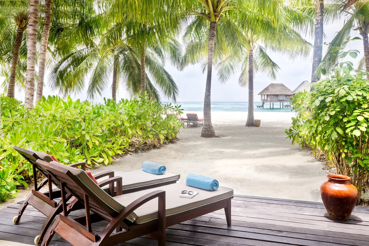 A Deluxe room’s wooden terrace, with 2 loungers and the sandy path through the green to the sea.