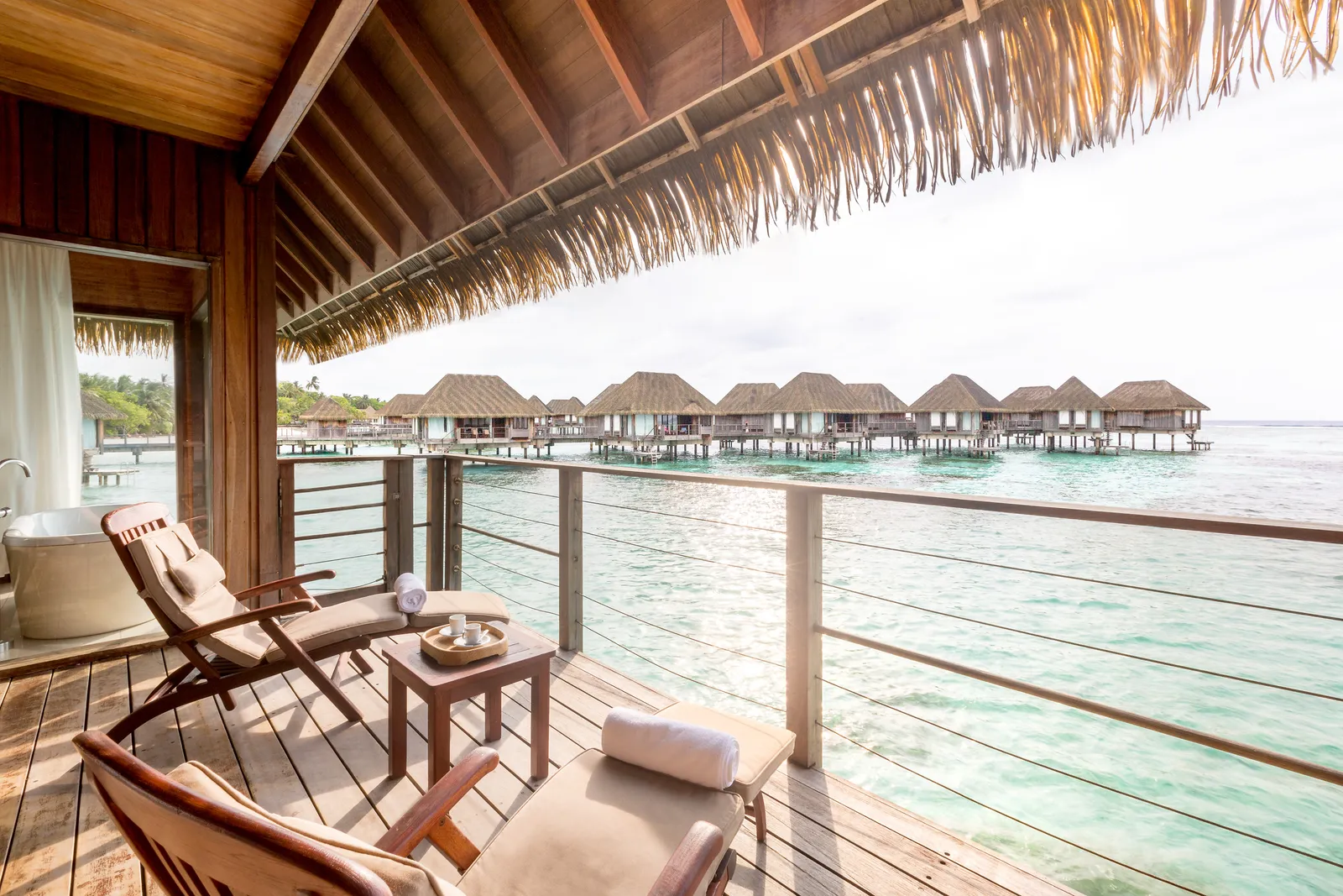 A family overwater suite’s deck, with the loungers, the tub and the row of other suites across the lagoon.