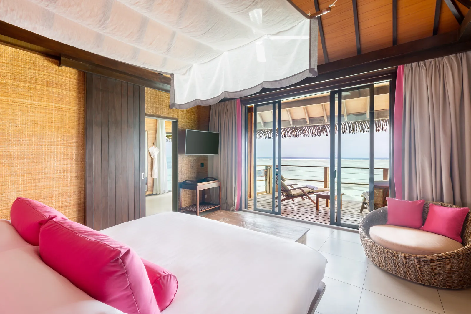 A family overwater suite’s bedroom: the canopied bed, the fuchsia cushions and the glass doors onto the deck.