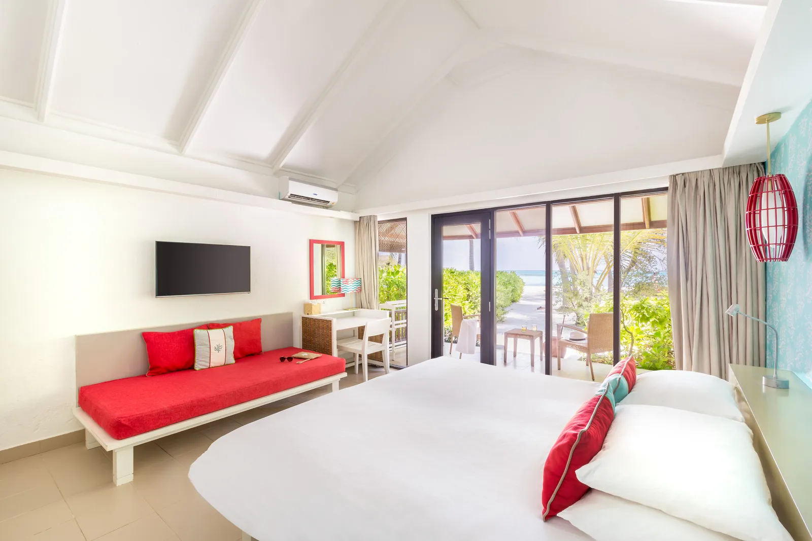 A beachfront Superior room: the white bed, the red sofa, the turquoise wall and the glass doors onto the terrace.