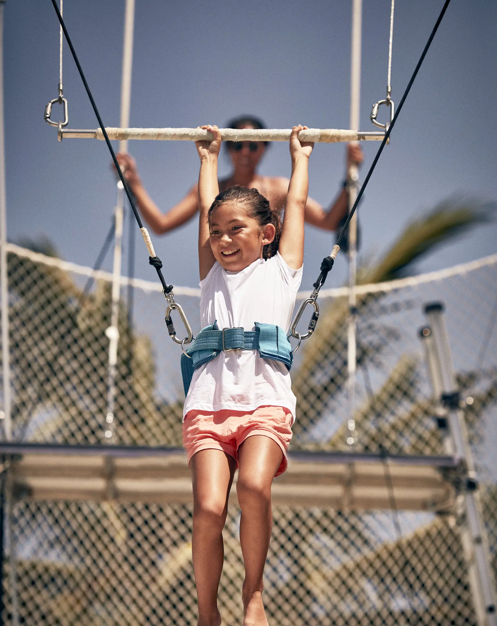 A girl in a harness hanging from the flying-trapeze bar, above the net.