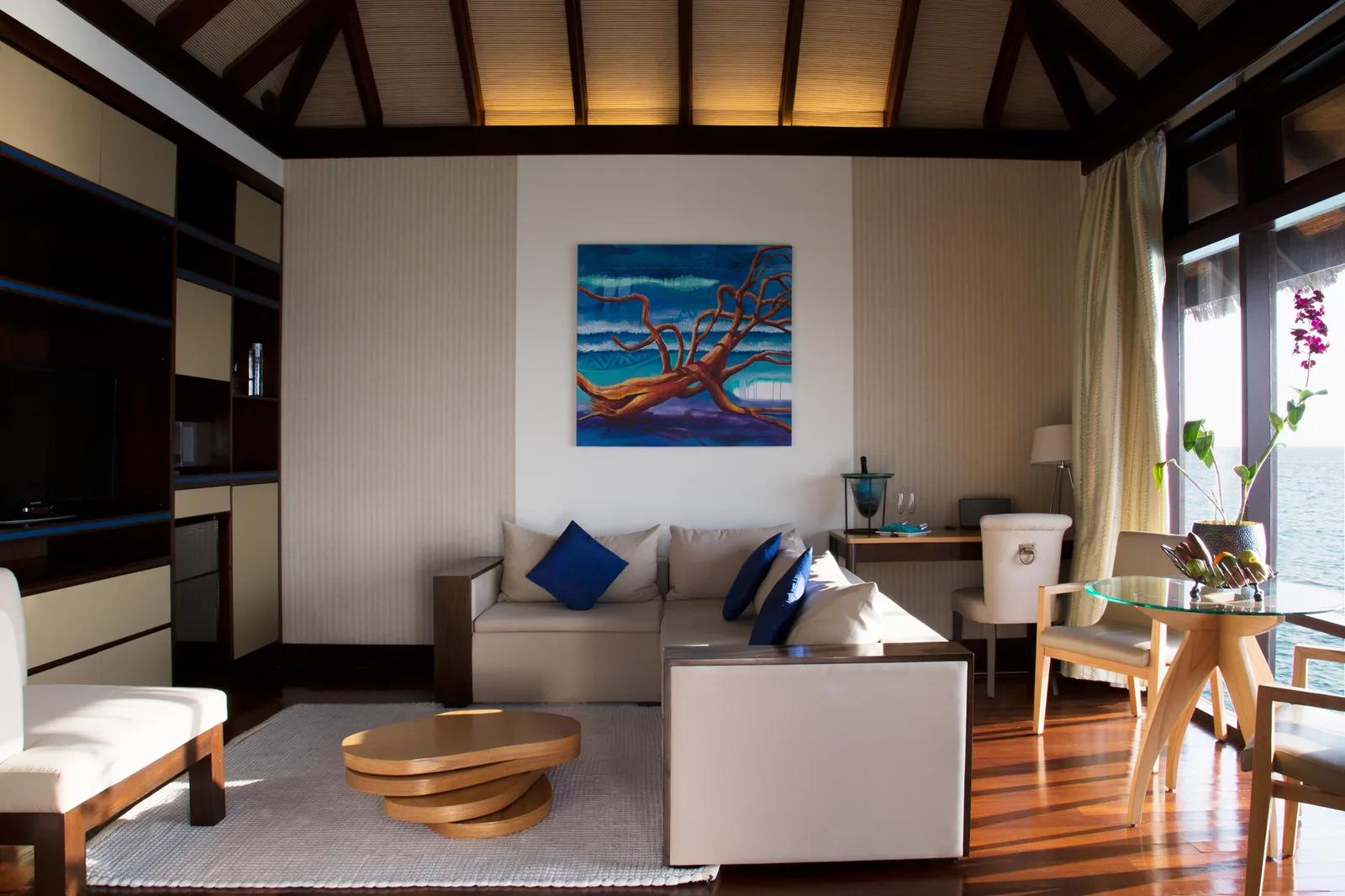 A Coco Residence living room: the white sofa with blue cushions, a brightly coloured painting and windows on the lagoon.