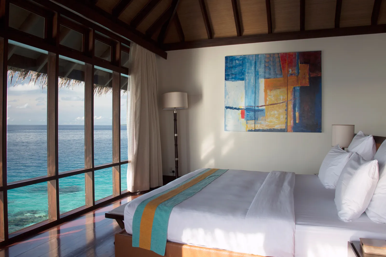 An Escape Water Villa bedroom: the white bed and floor-to-ceiling windows on the lagoon.