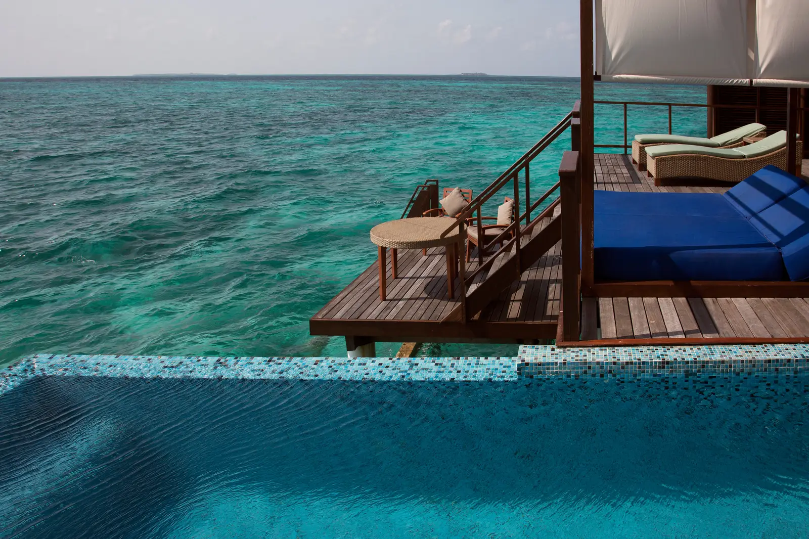 A Coco Residence’s deck: the infinity pool, the four-poster daybed with blue cushions and the lagoon to the horizon.
