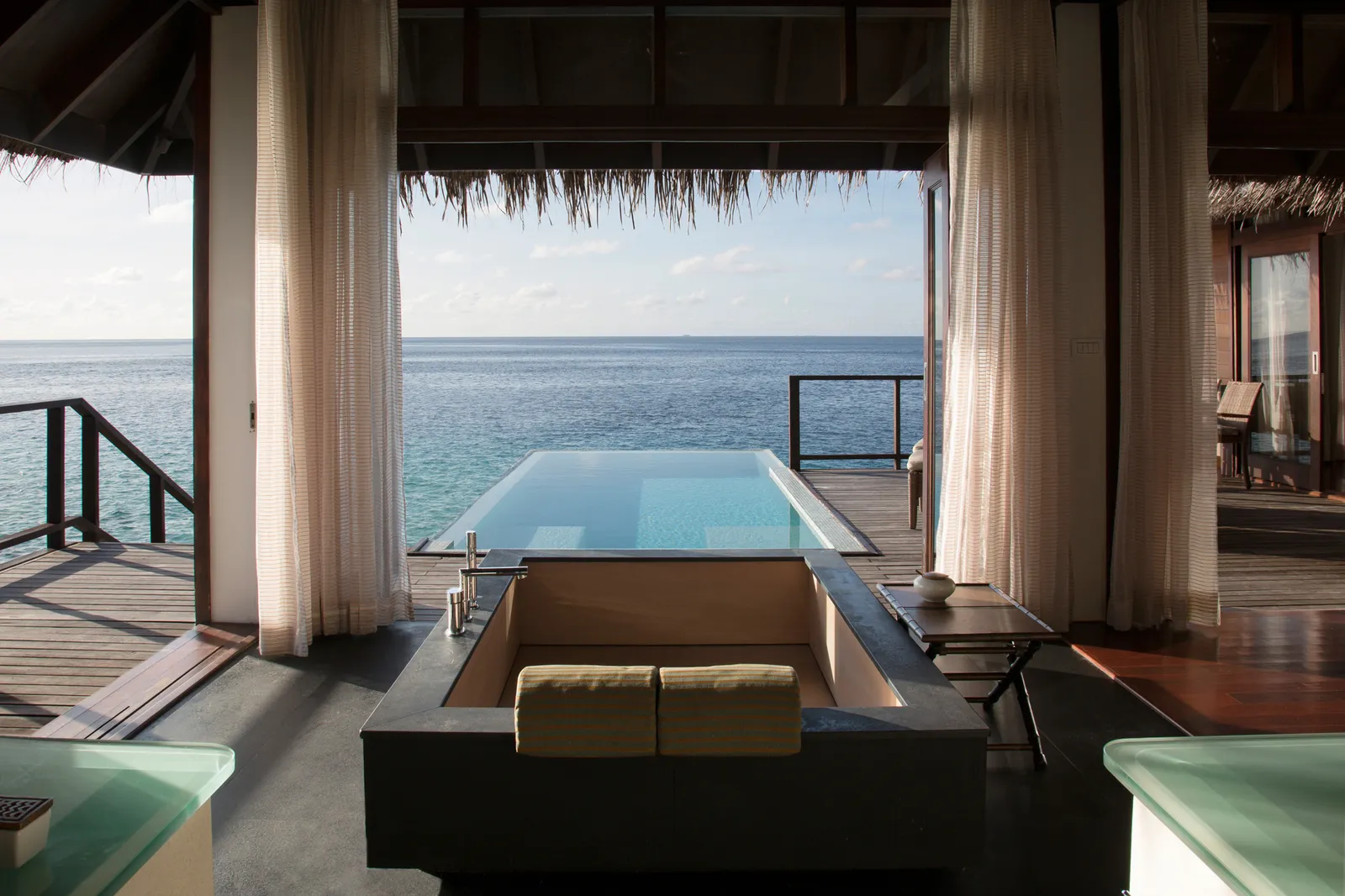 An Escape Water Villa with Pool from inside: the bathtub facing the open curtains, the infinity pool and the lagoon.