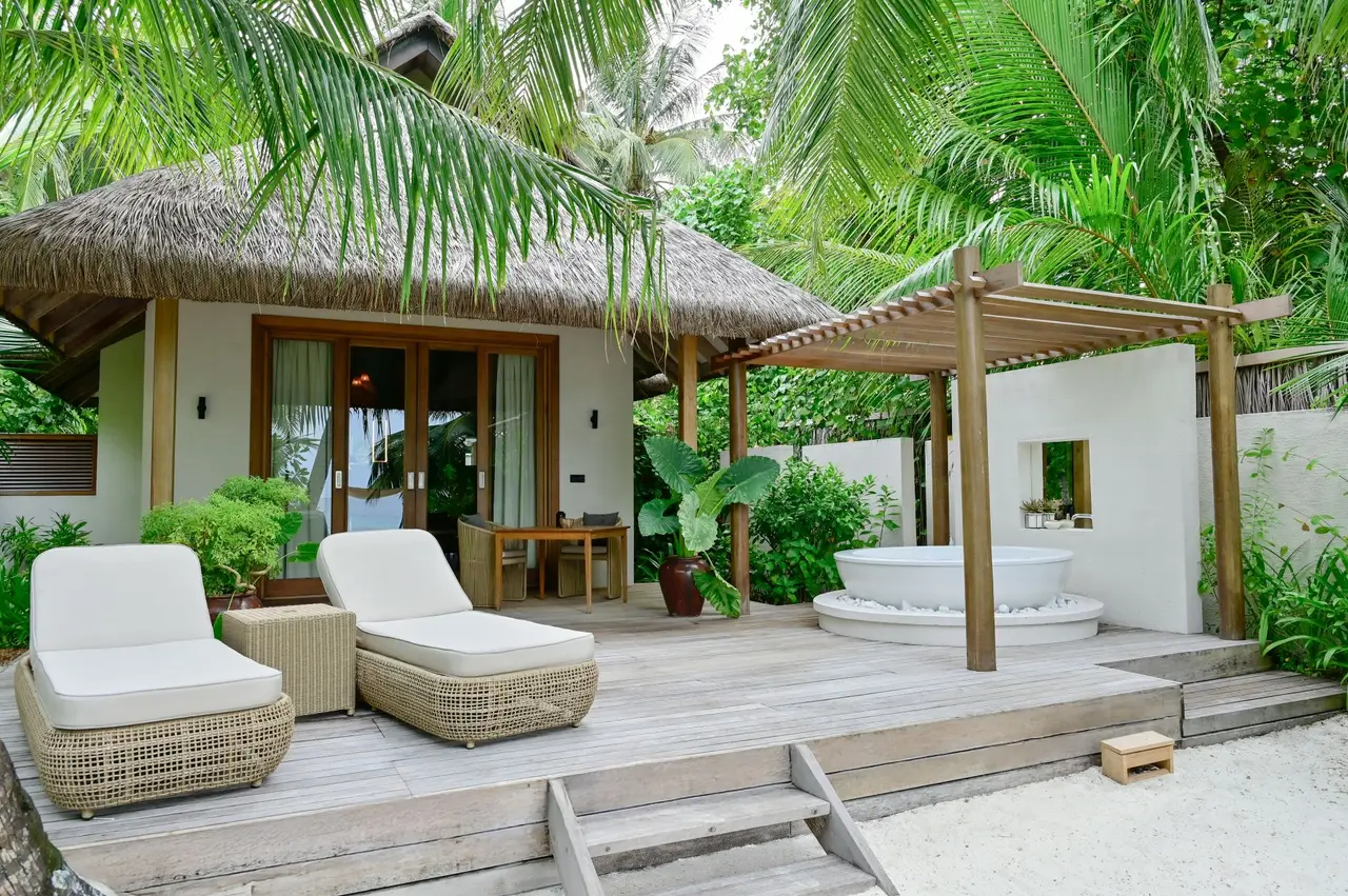 The Grand Premier Beach Villa with Pool: the deck with white loungers, the pergola and the outdoor bath among the greenery.