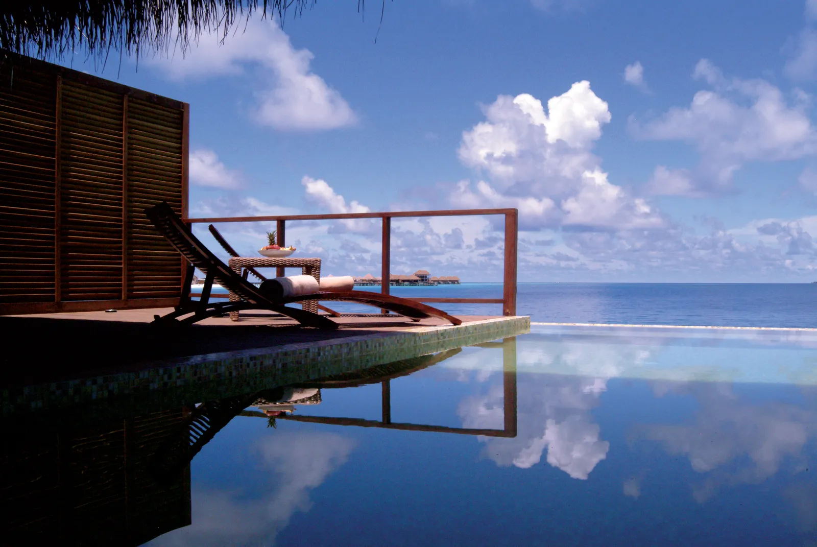 A Water Villa with Pool’s deck: a lounger in the sun and the infinity pool mirroring the sky and the ocean.