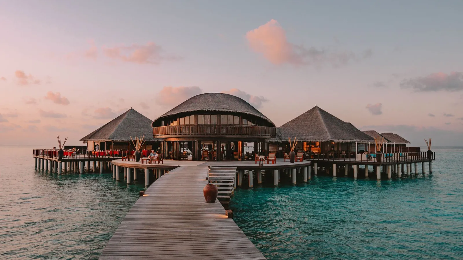 The timber jetty out to Stars, the restaurant on the lagoon, at sunset, its lights on under the domed roofs.