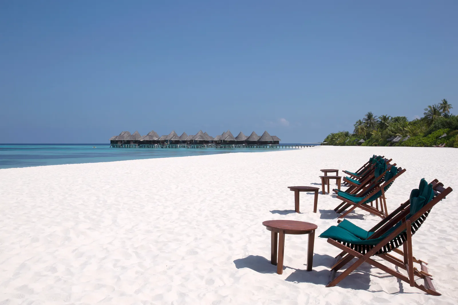 Wooden deckchairs on the Beach Bar’s white sand, with the water villas on the horizon.