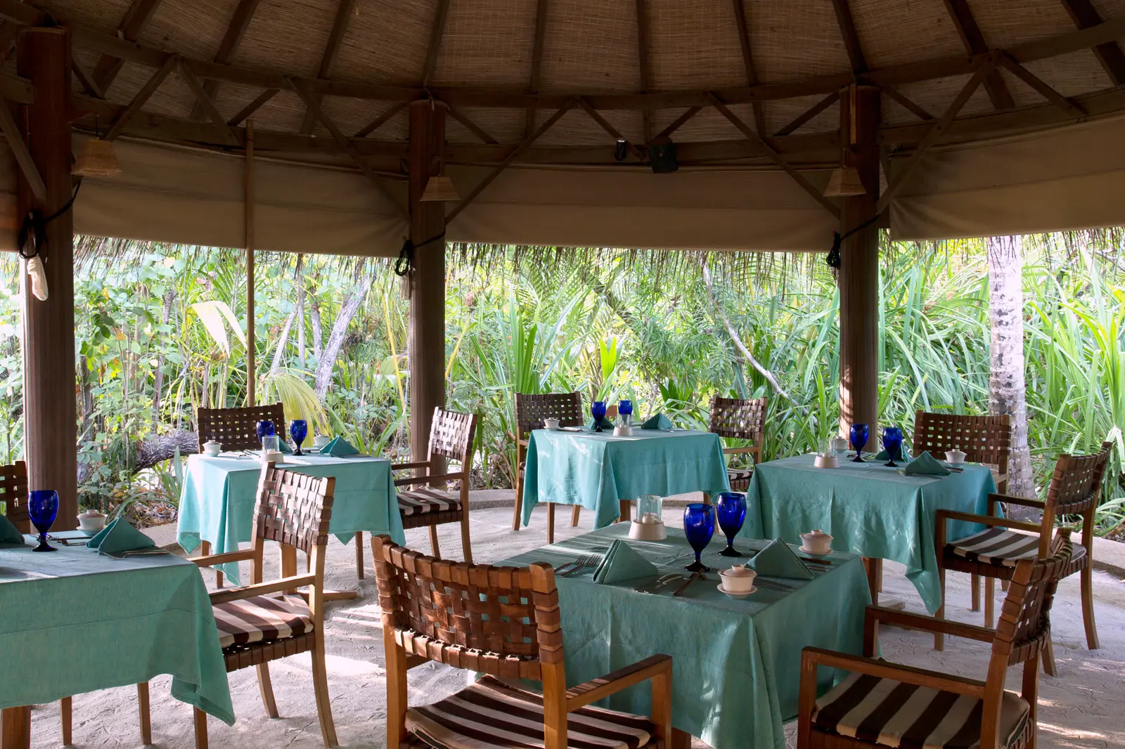 Cornus’s laid tables under a timber pavilion, with a sand floor and greenery around.
