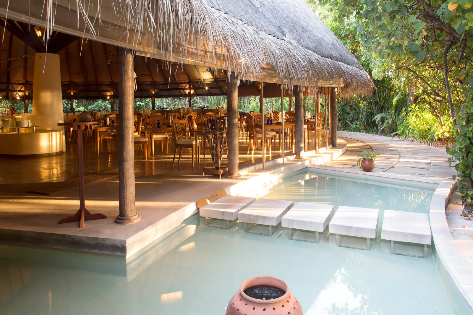 Cowrie, the main restaurant, under its thatched roof, with pools of water and stepping stones in front of the tables.