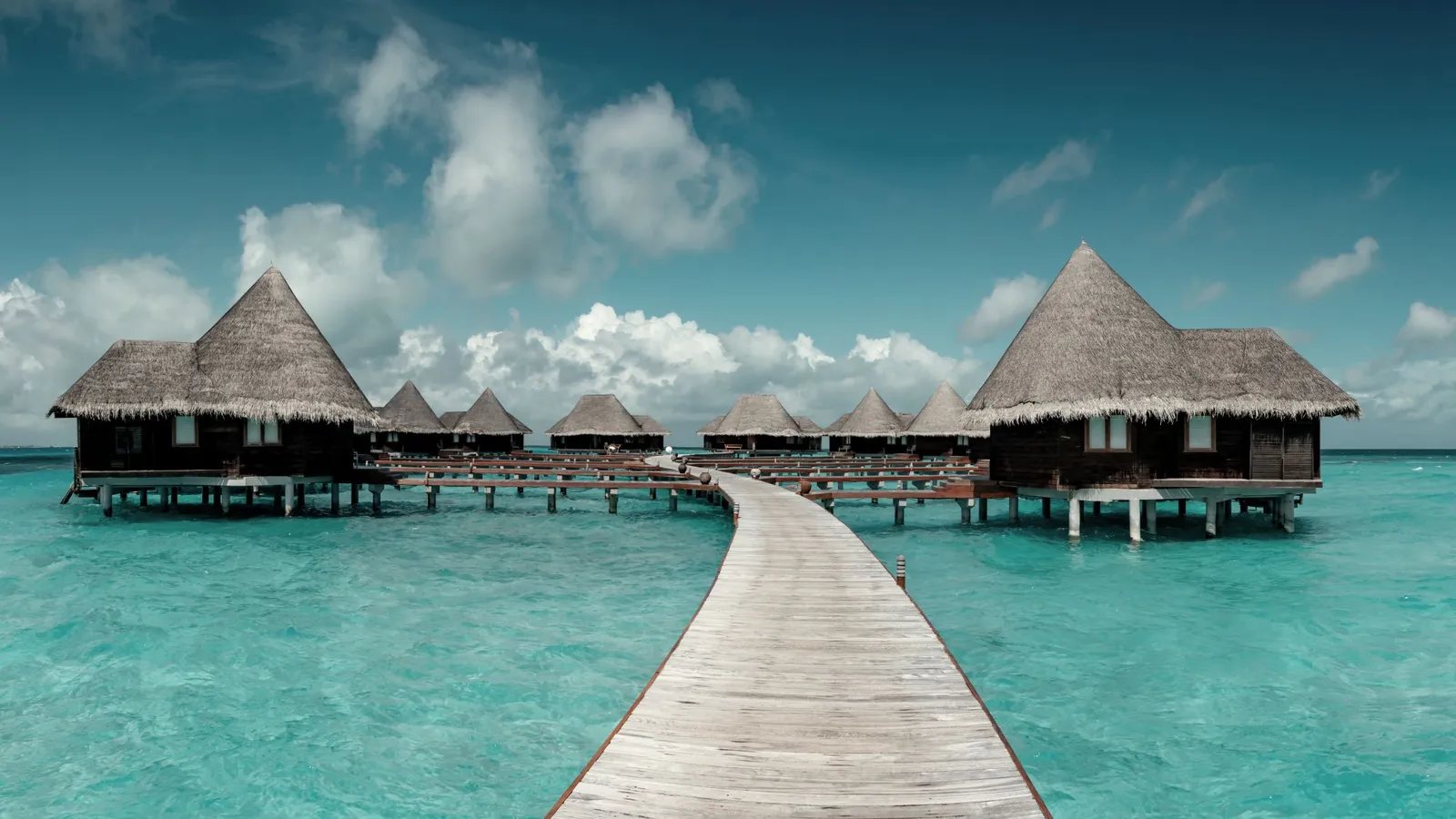 The timber walkway out to the thatched water villas, over the clear lagoon.