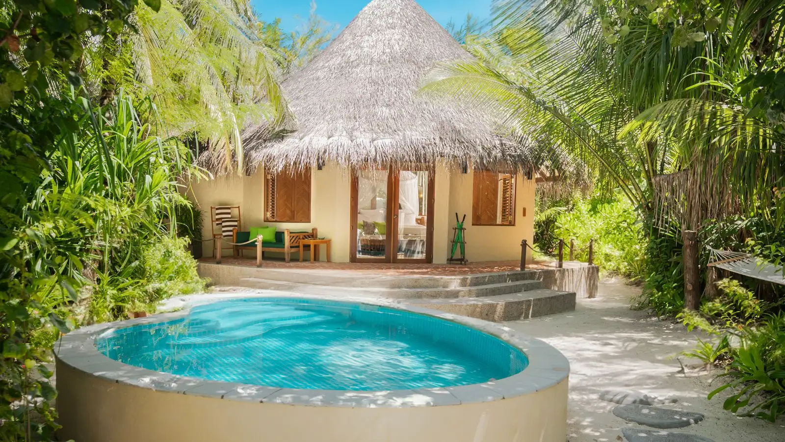 The round pool of a Deluxe Pool Villa in front of the thatched villa, in the greenery.