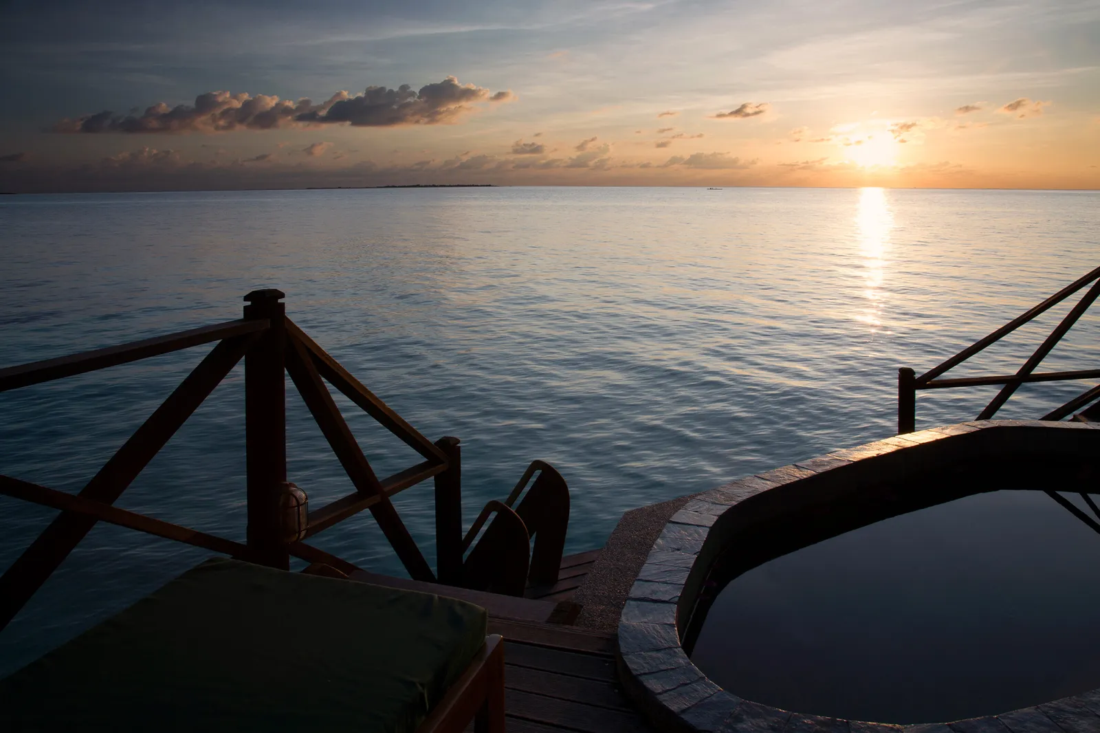 A Lagoon Villa’s deck at sunset, with its sunken pool and the sun low over the ocean.