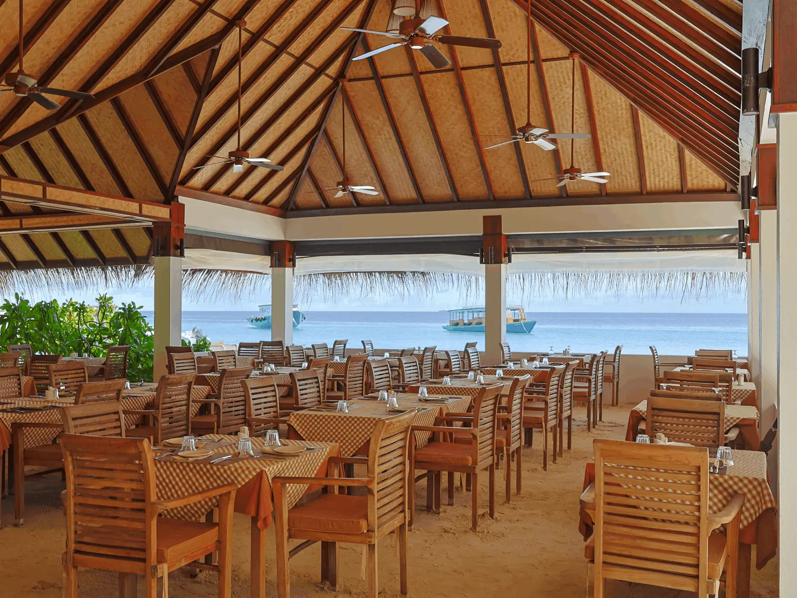 Azure Lagoona’s dining room under its timber roof, the tables laid on the sand and the lagoon beyond the columns.