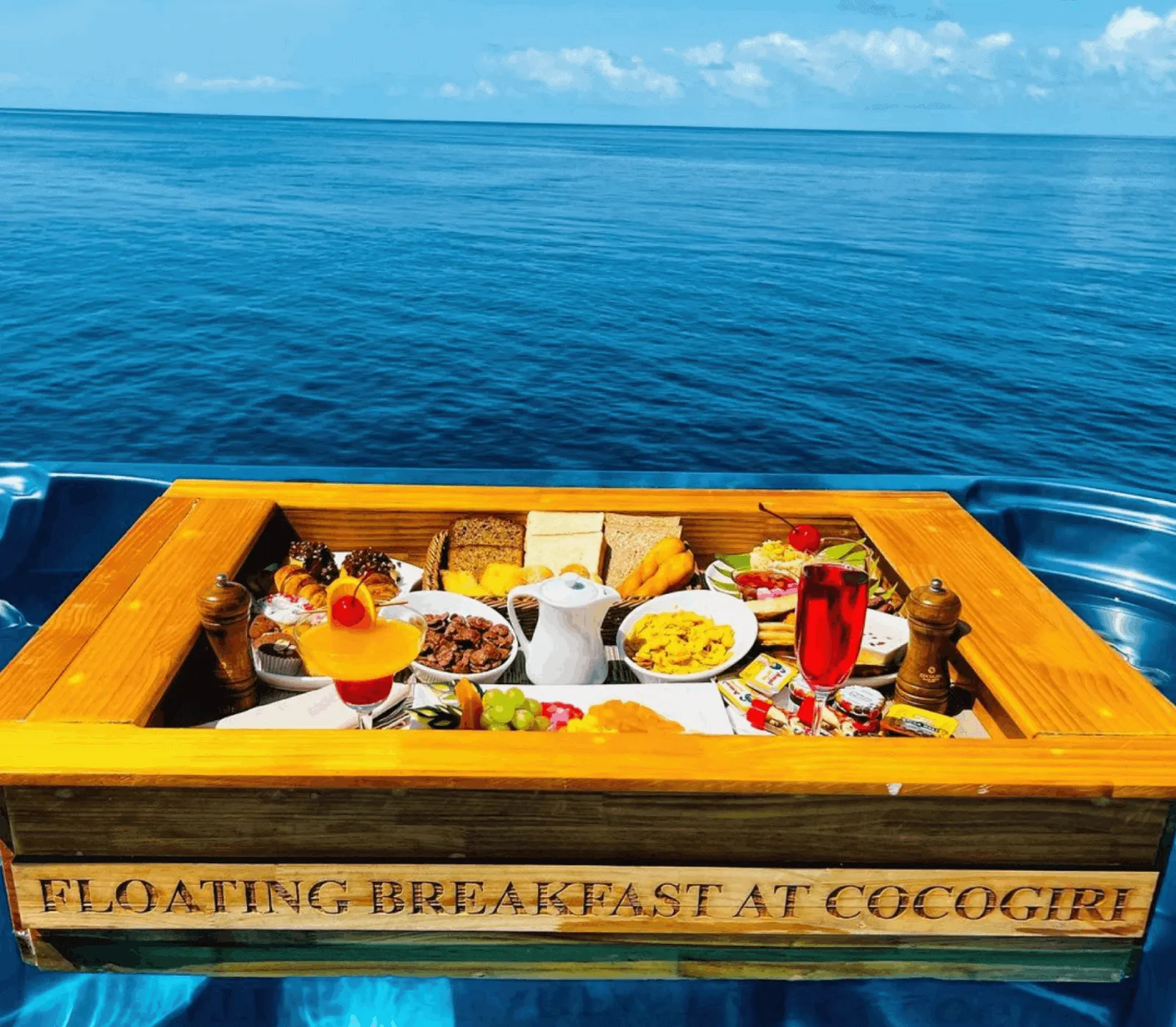 The floating breakfast tray, carved with Cocogiri’s name, in a villa’s pool with the sea behind.