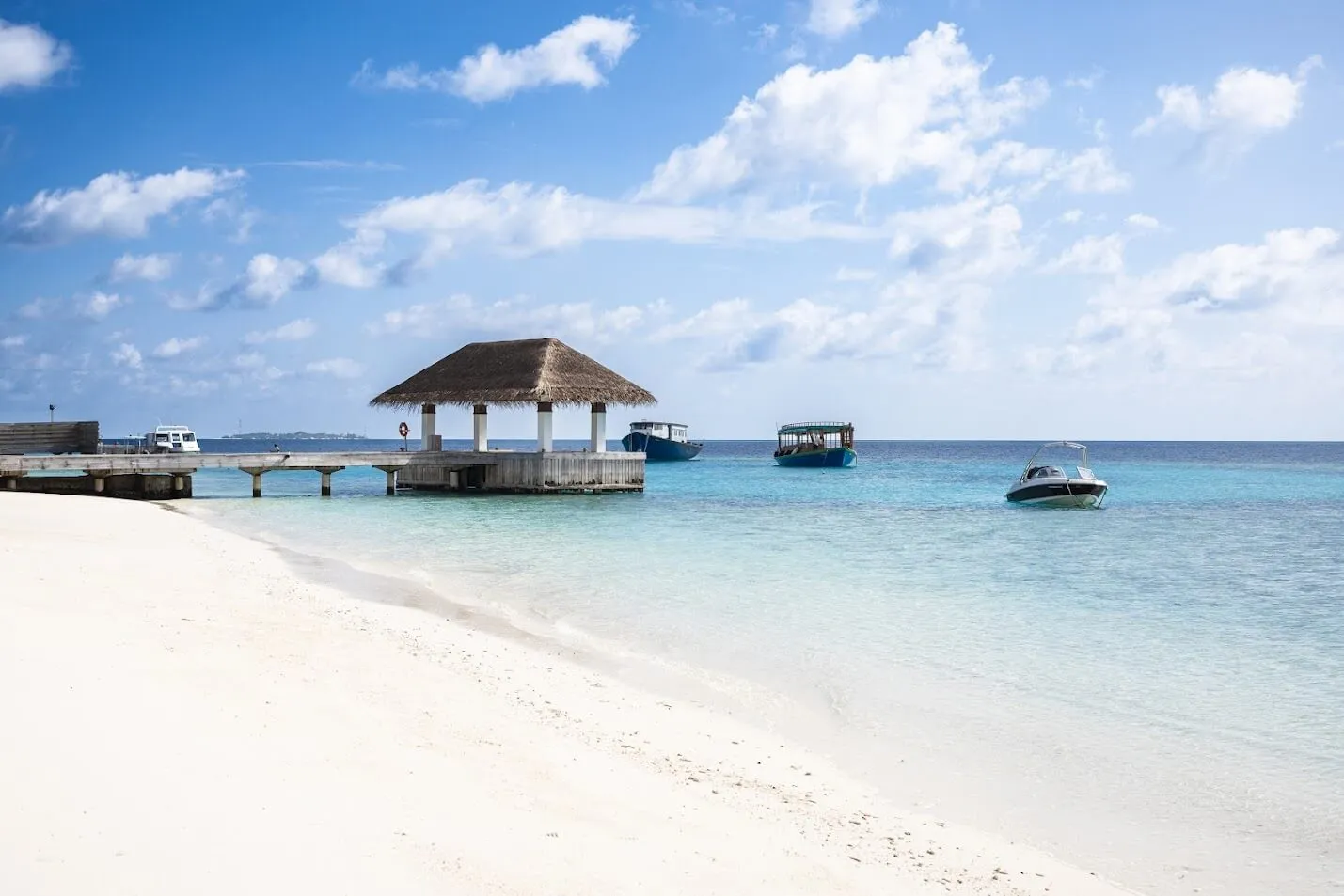 The white beach running down to the jetty and its wooden pavilion, with boats moored in the lagoon.