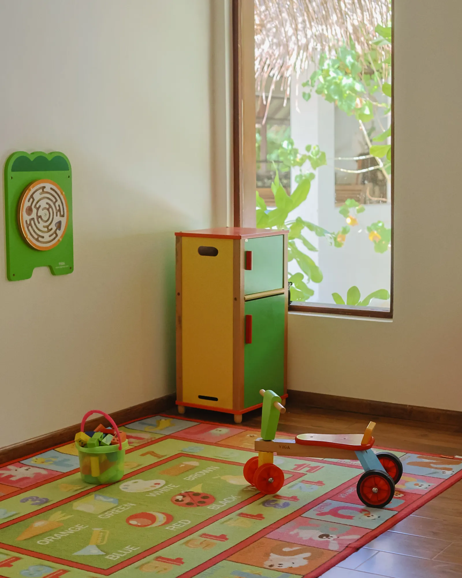 The kids’ club room, with a toy kitchen, a tricycle and a bright play mat.