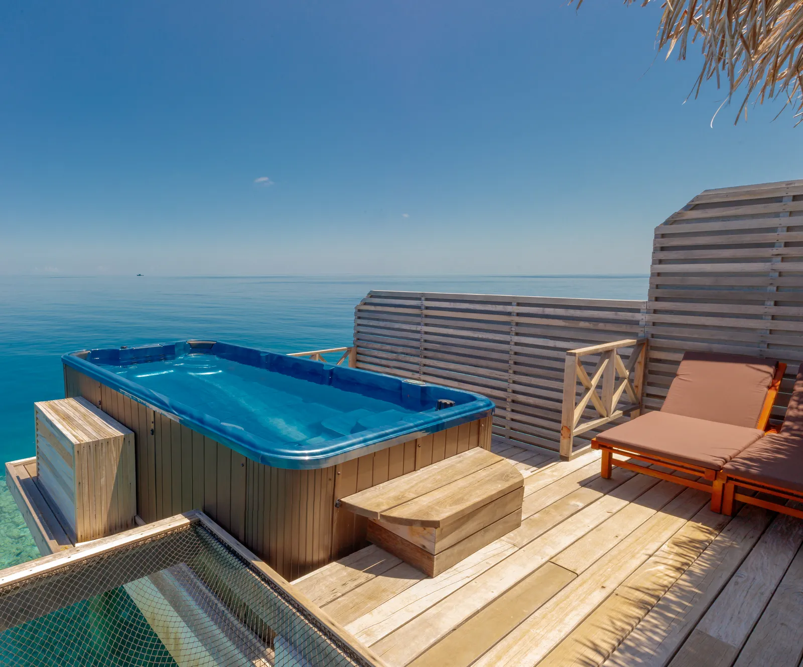 A Pool Jacuzzi Water Villa’s deck: the rectangular pool jacuzzi on the timber deck, a lounger and the sea.