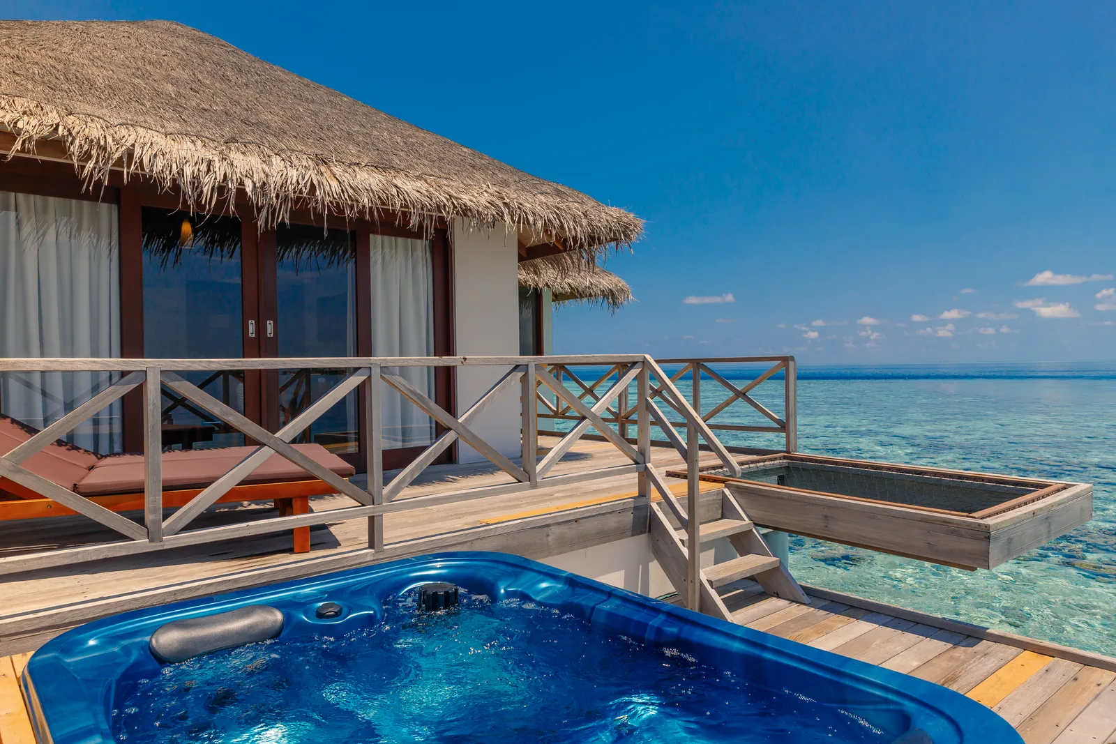 A thatched Standard Jacuzzi Water Villa: the blue jacuzzi on the deck and the steps down to the lagoon.