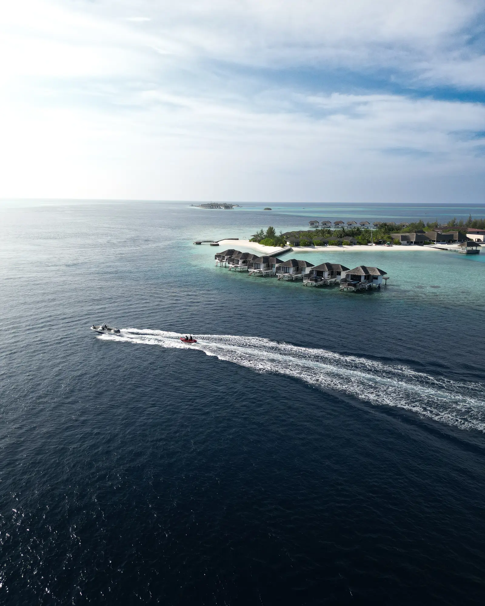 A speedboat leaving its wake on the dark sea, heading for the island and its water villas.
