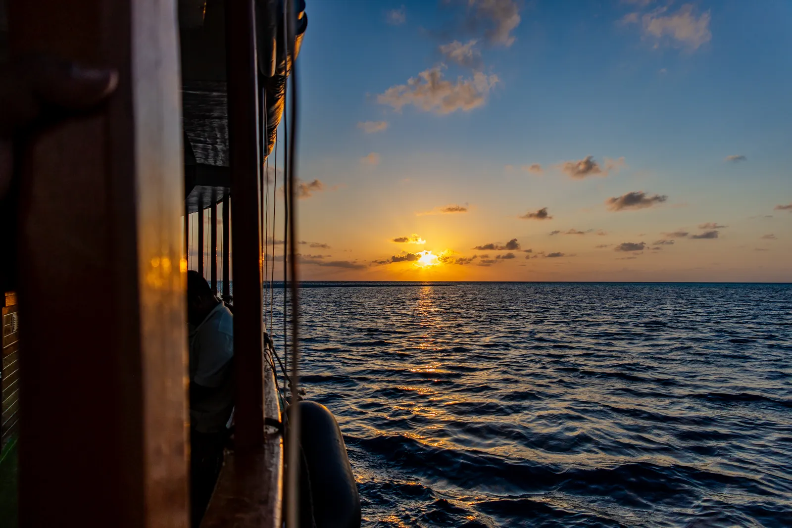 The sun setting over the sea, seen from the wooden side of a boat.