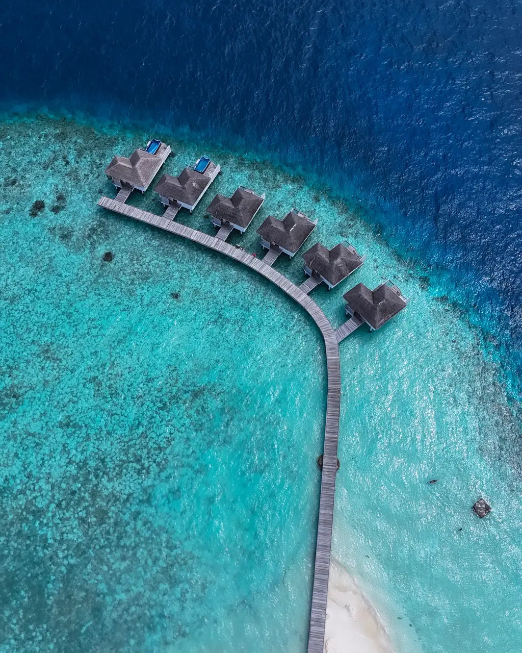 The water villa walkway seen from above, leaving the beach and curving towards the edge of the reef.