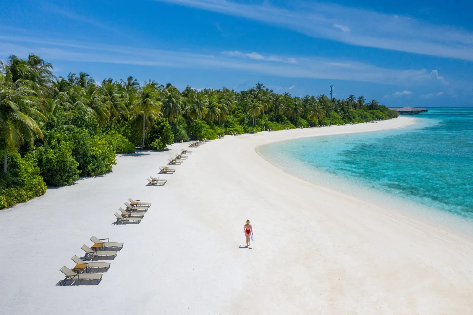 The long white beach with loungers under the palms, a woman walking along the shore