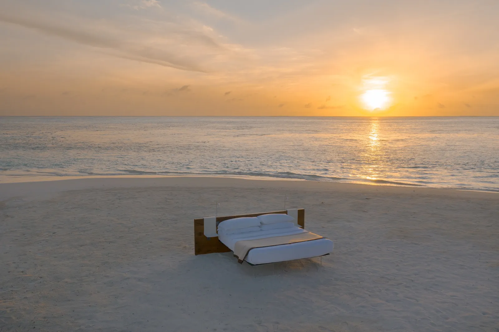 A bed on the sand facing the sea, the sun going down