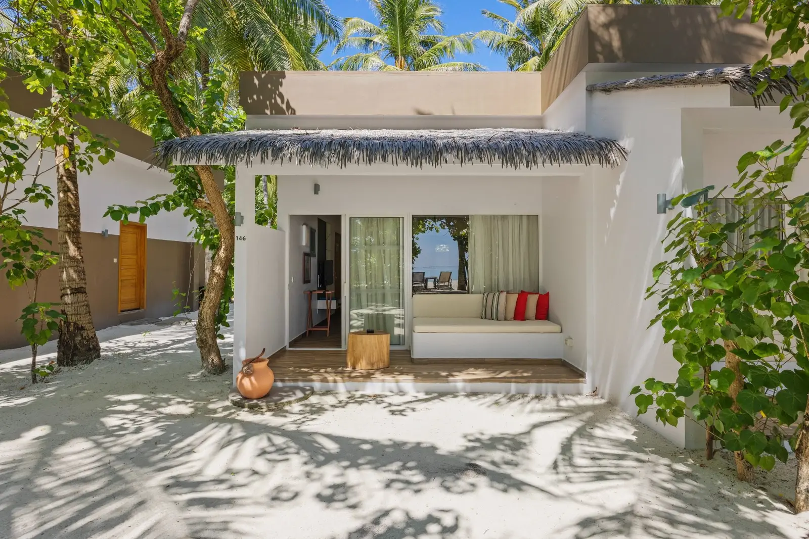 A Beach Villa: the veranda with its daybed, white walls and a thatched roof among the trees