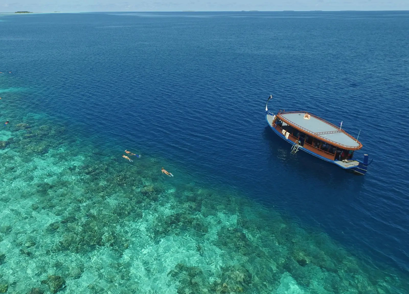 A dhoni boat at the edge of the reef, snorkellers in the water