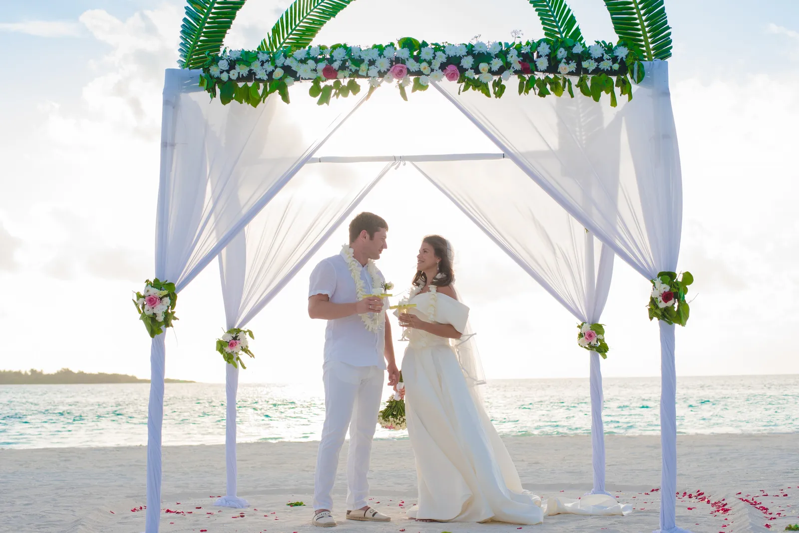 A bride and groom under the arch of flowers and drapes on the beach