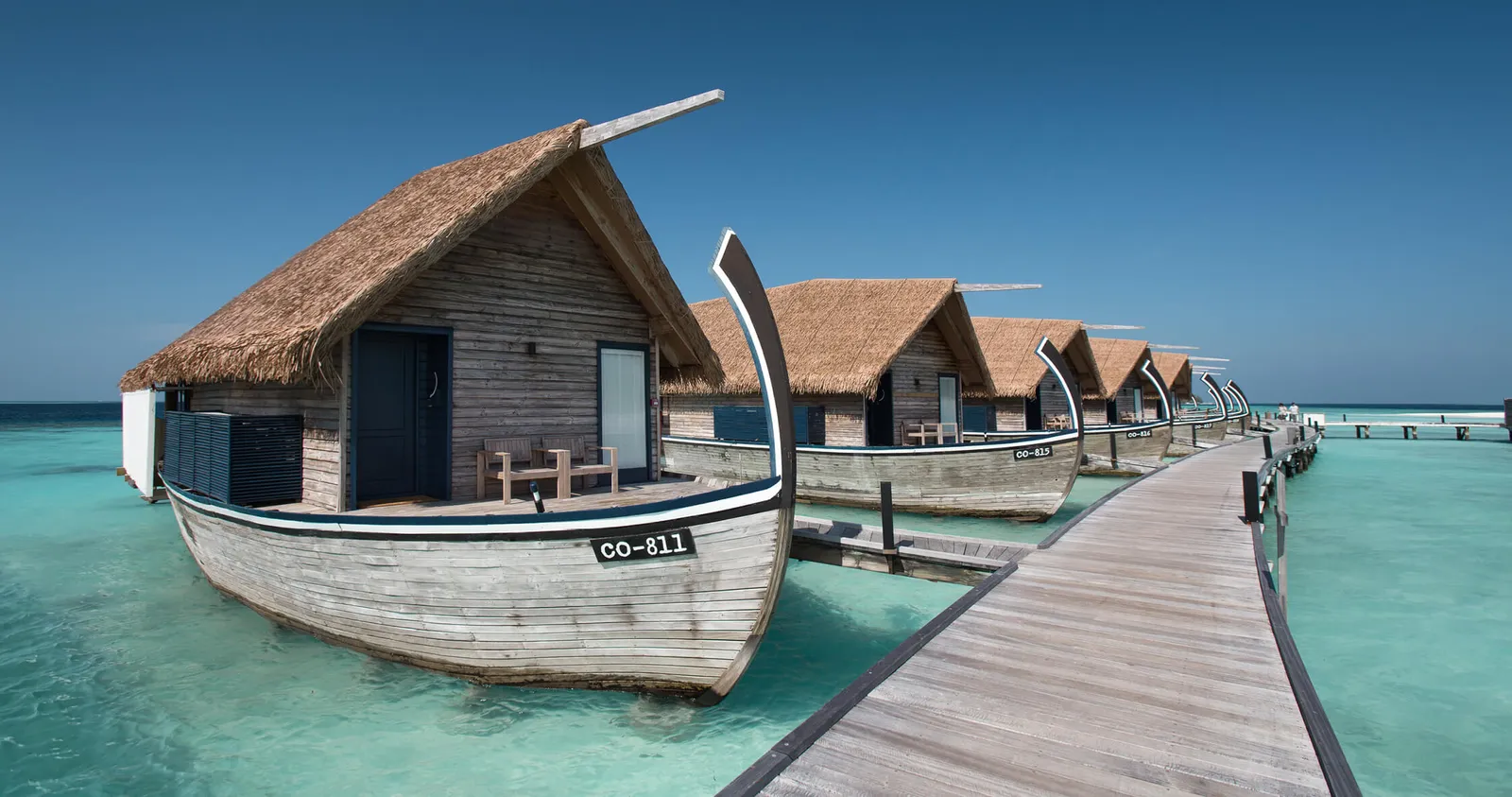 A Dhoni Water Villa, shaped like a traditional Maldivian boat, beside the wooden jetty over the lagoon