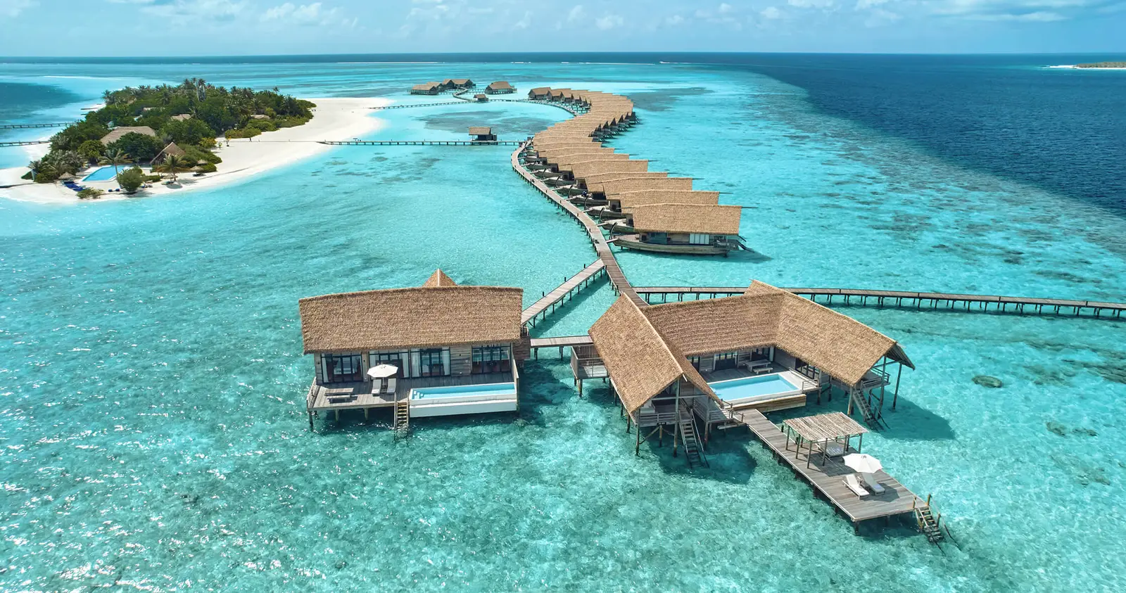 The island from above, with the pool villas over the water in front and the reef around it