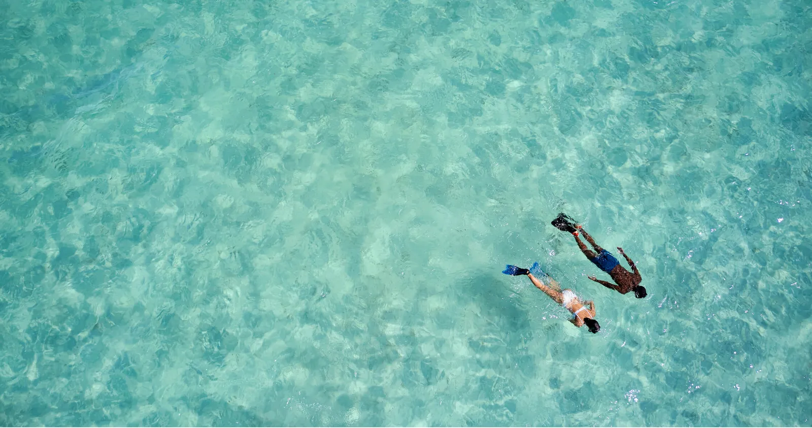 2 people snorkelling in the turquoise lagoon, seen from above