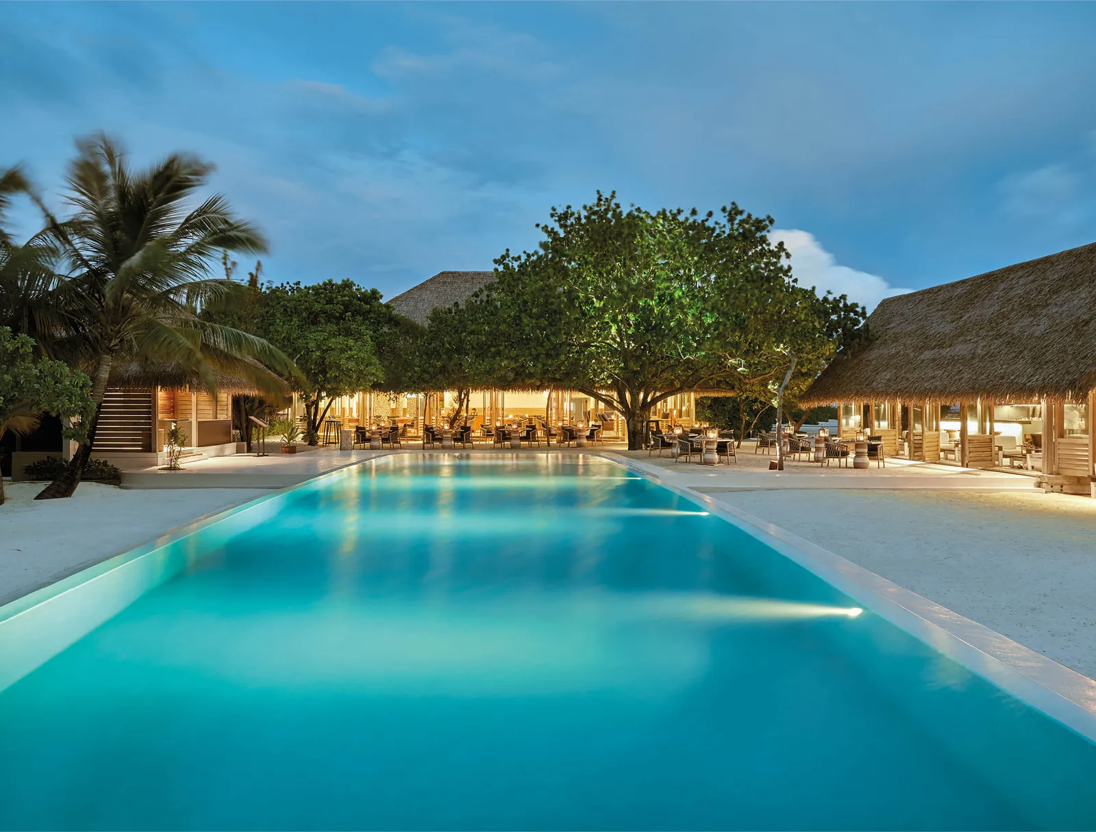 The main pool lit in the evening, with the restaurant under the trees