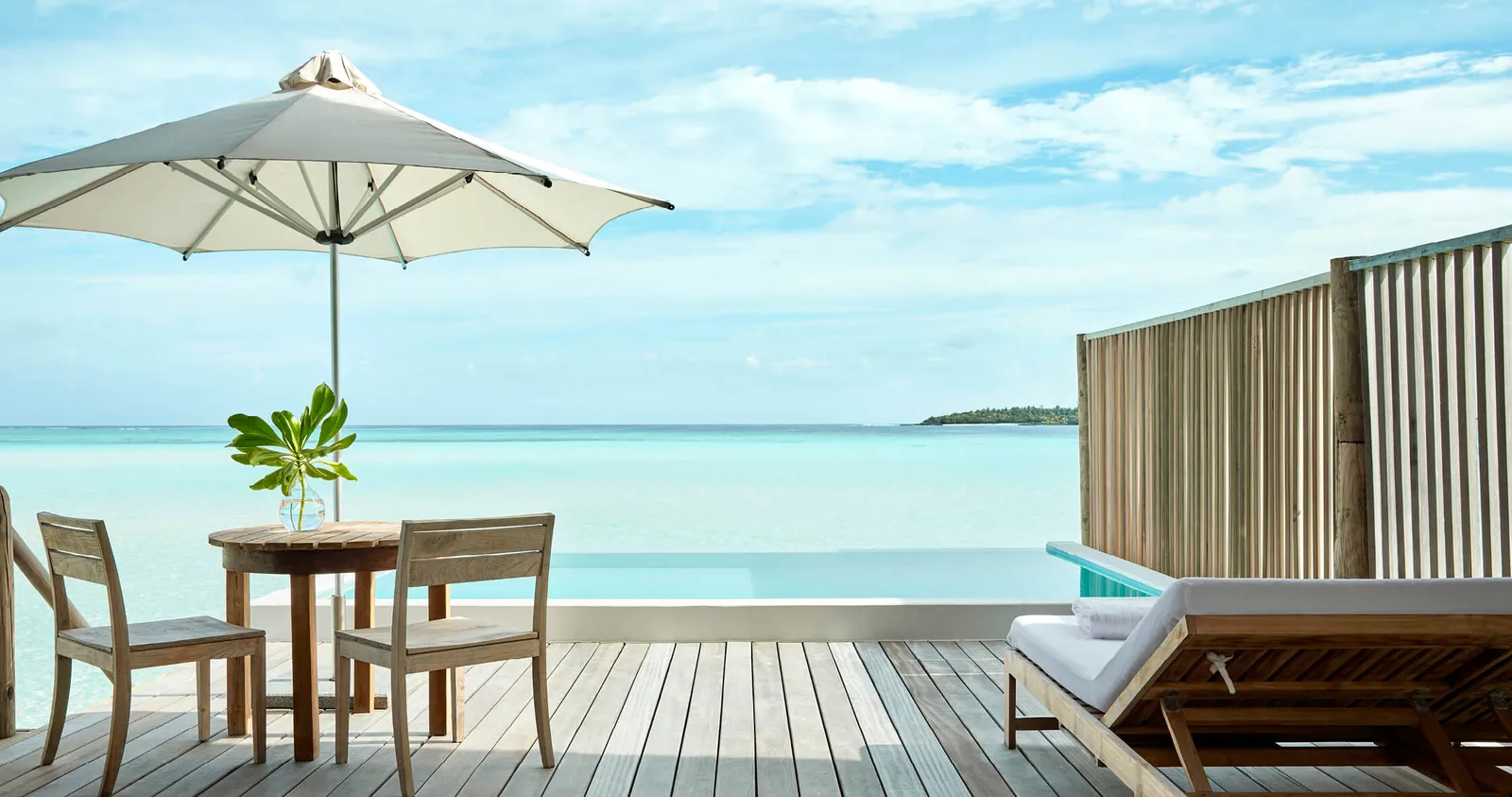 The deck of an overwater pool villa, a table under the umbrella and the lagoon beyond