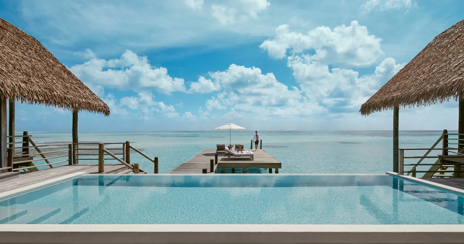 The infinity pool of a COMO Sunrise Villa, between 2 thatched roofs, facing the jetty and the sea